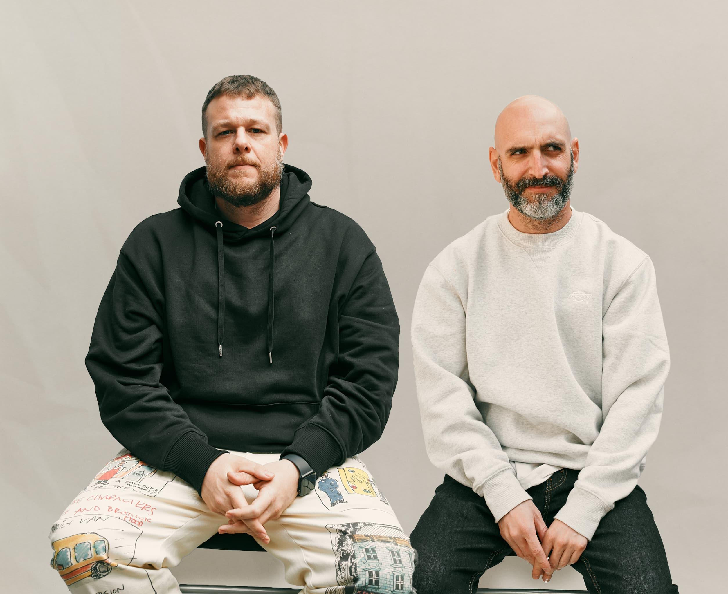Two people seated side by side, one in a black hoodie and one in a light sweatshirt.