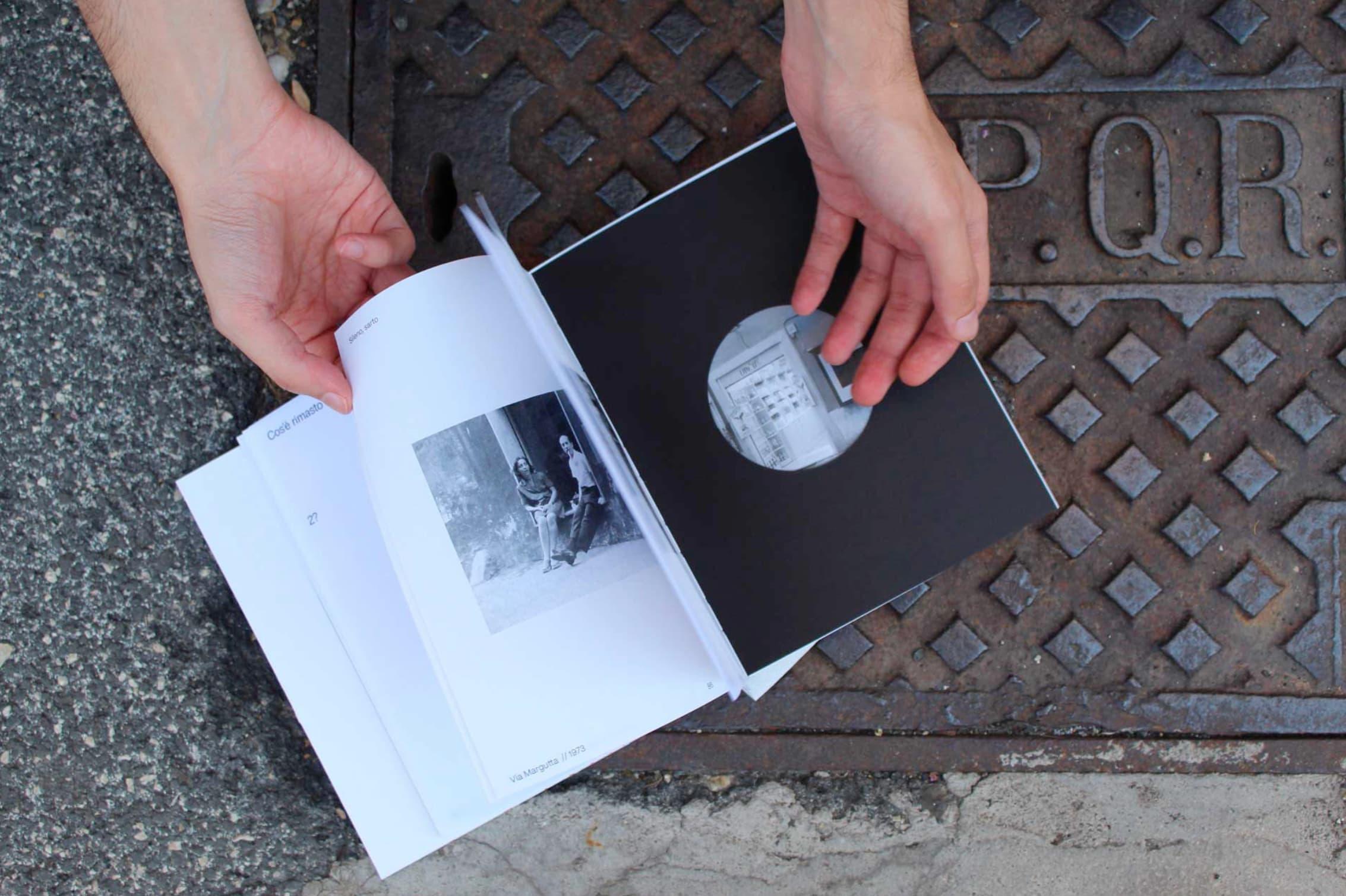Hands holding an open book with a black-and-white photograph and a black page with a circular image.