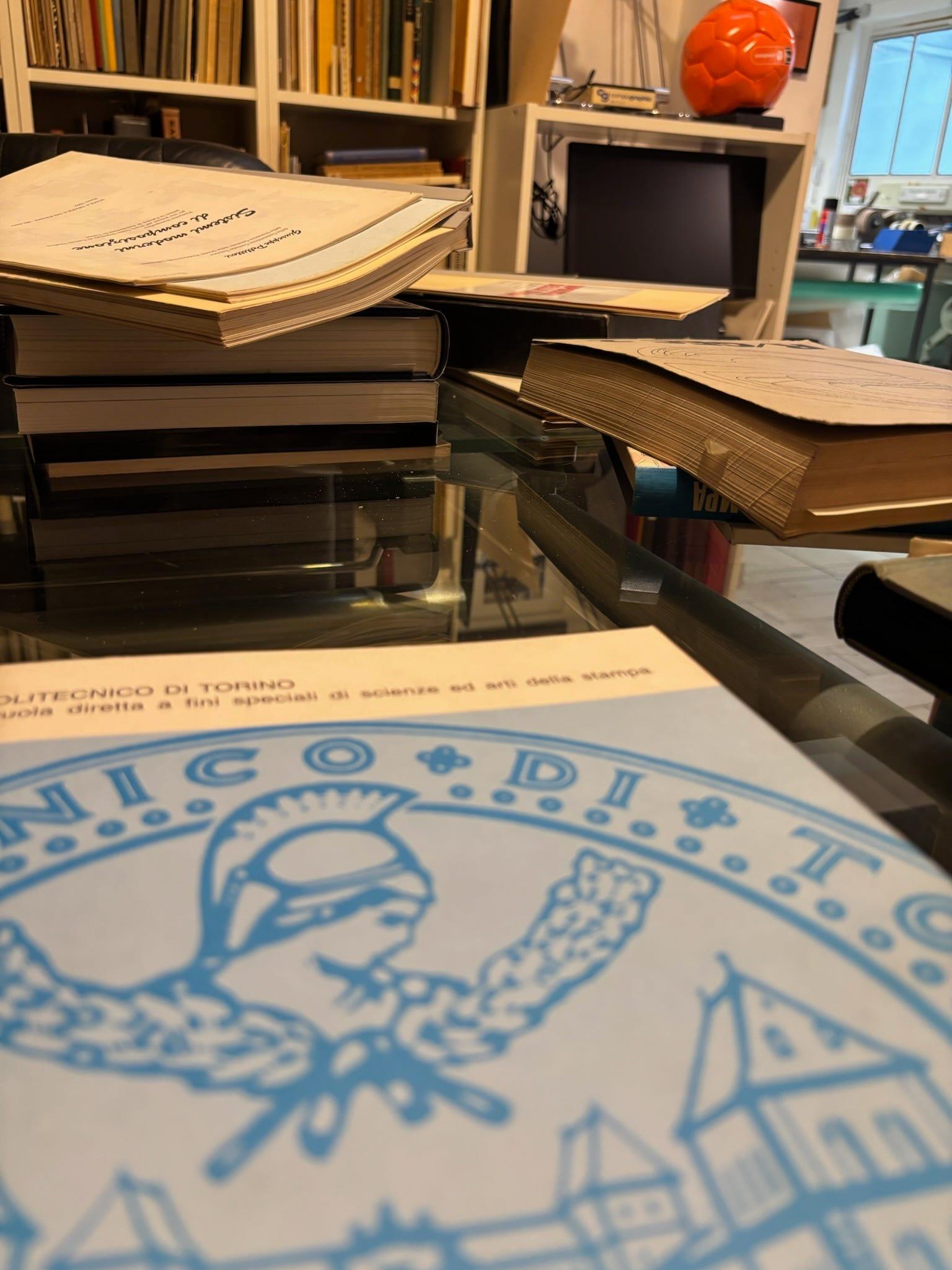 Stacked books and paper files on a glass table at the Library of the Politecnico di Torino.