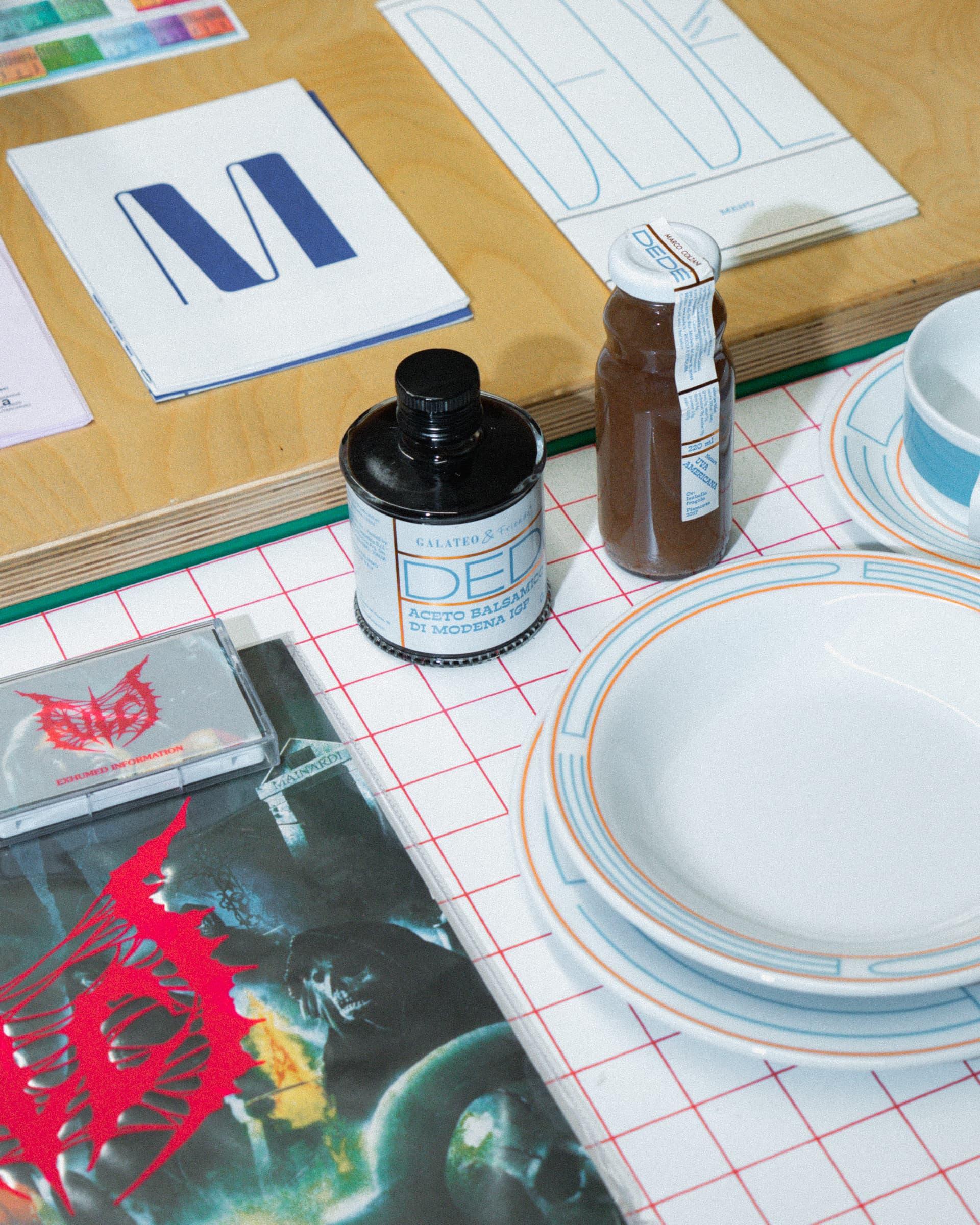 Printed materials, plates and bottles on a grid-patterned tablecloth.
