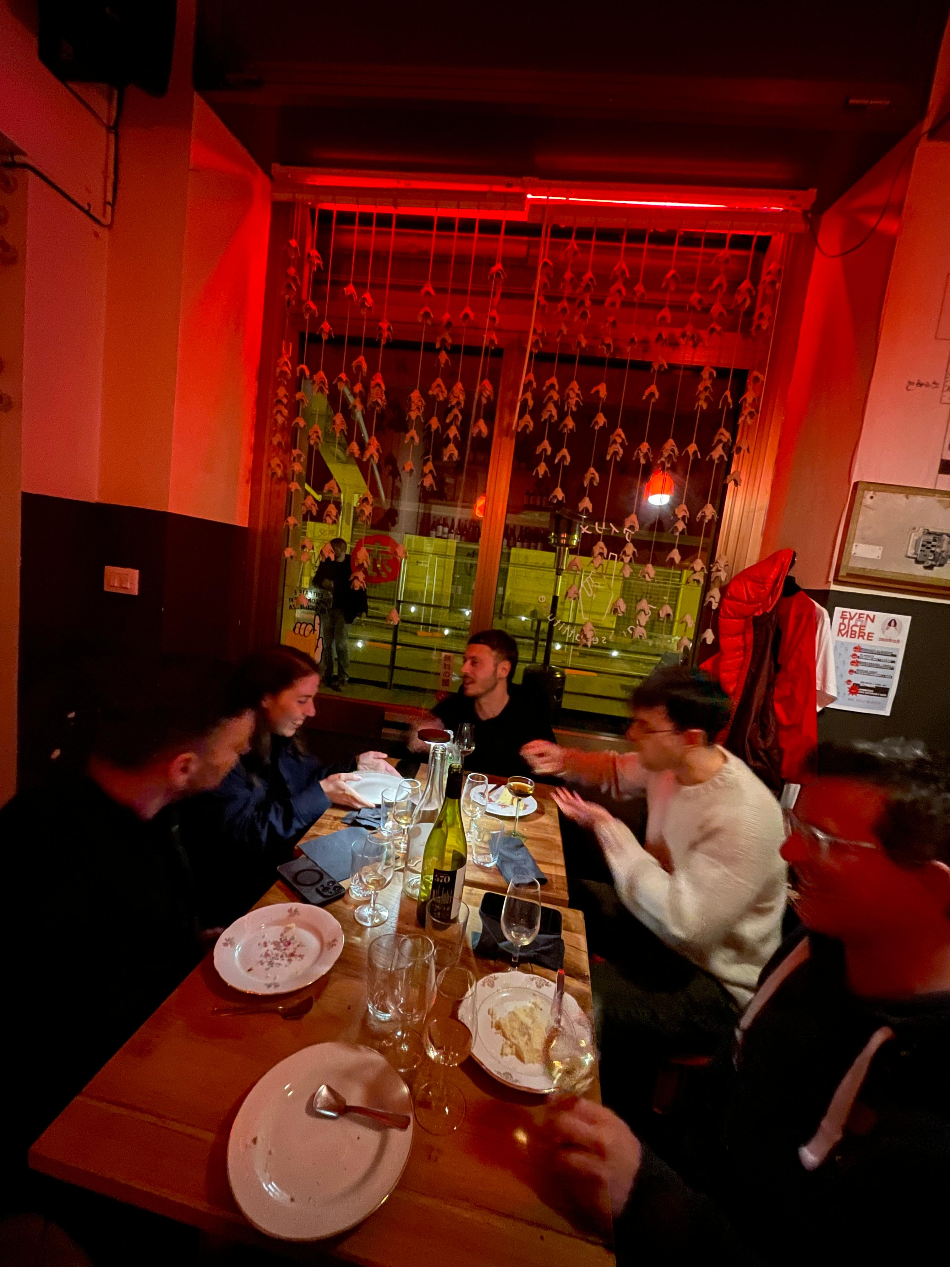 People dining around a long table in a red-lit restaurant.
