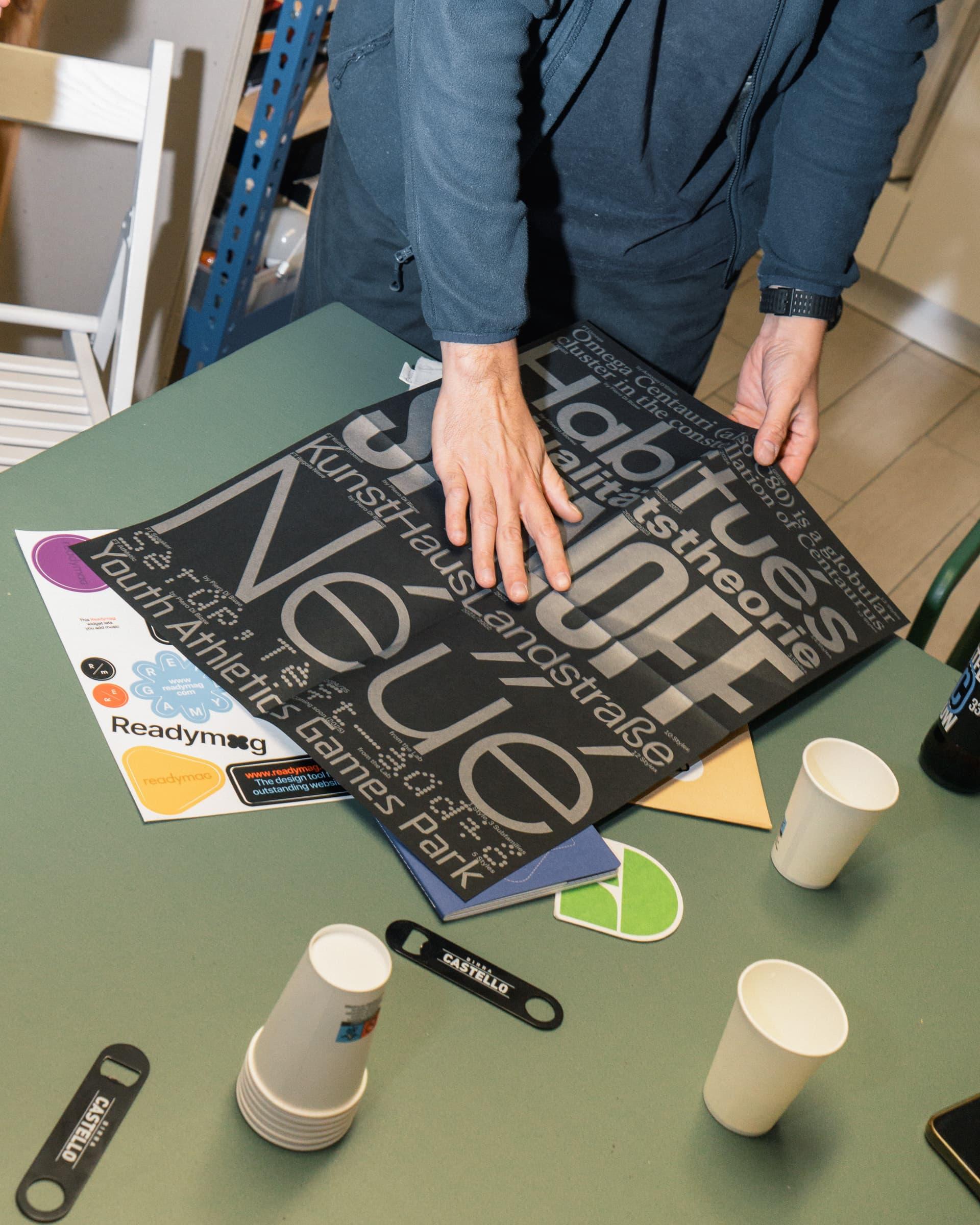 Attendee placing a black typographic poster on a green table.