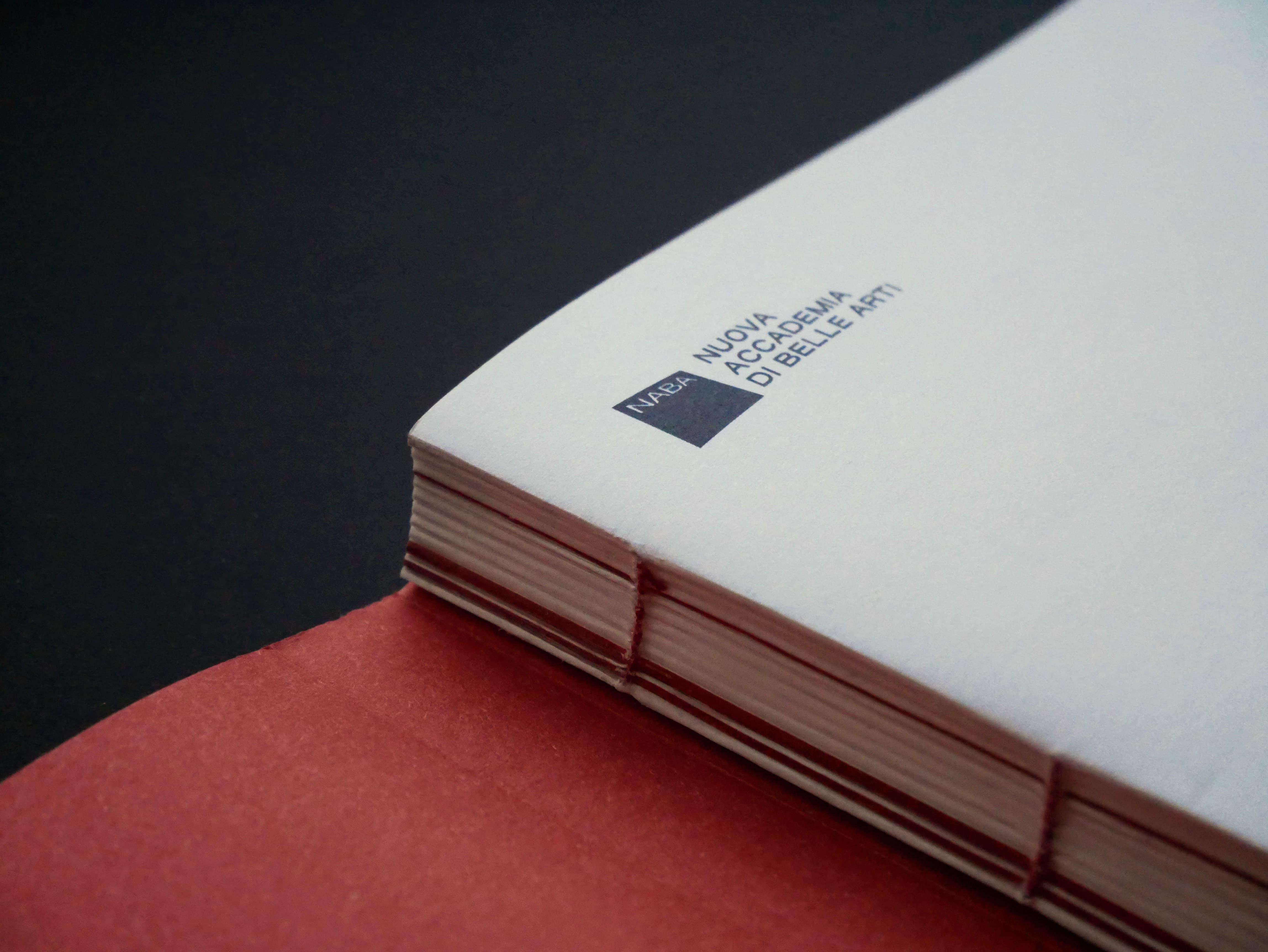 Close-up of the white Kraftoria thesis book on a red-orange cover, printed with the NABA Nuova Accademia di Belle Arti mark.