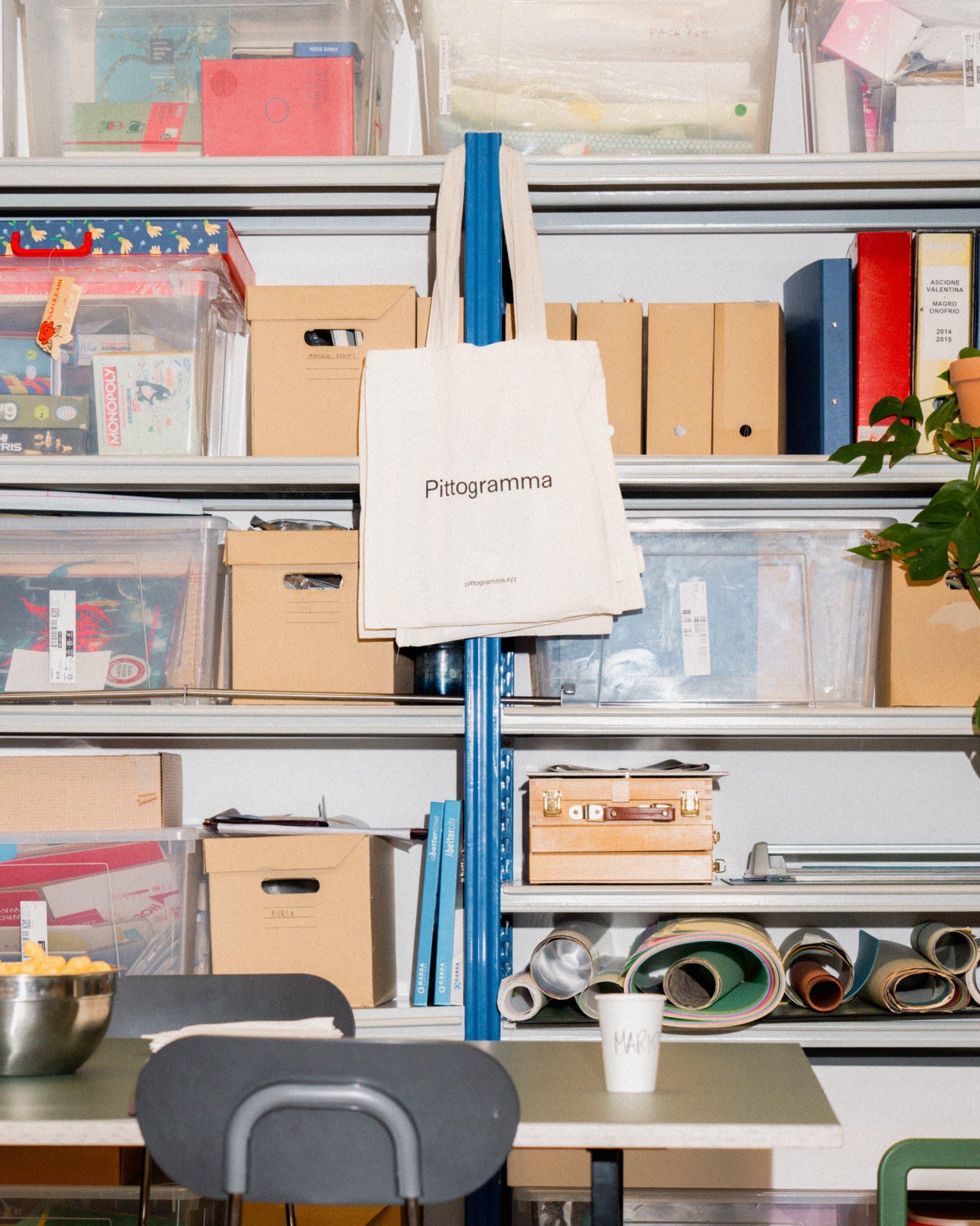 Pittogramma tote bag hanging from shelving filled with studio files and material rolls.