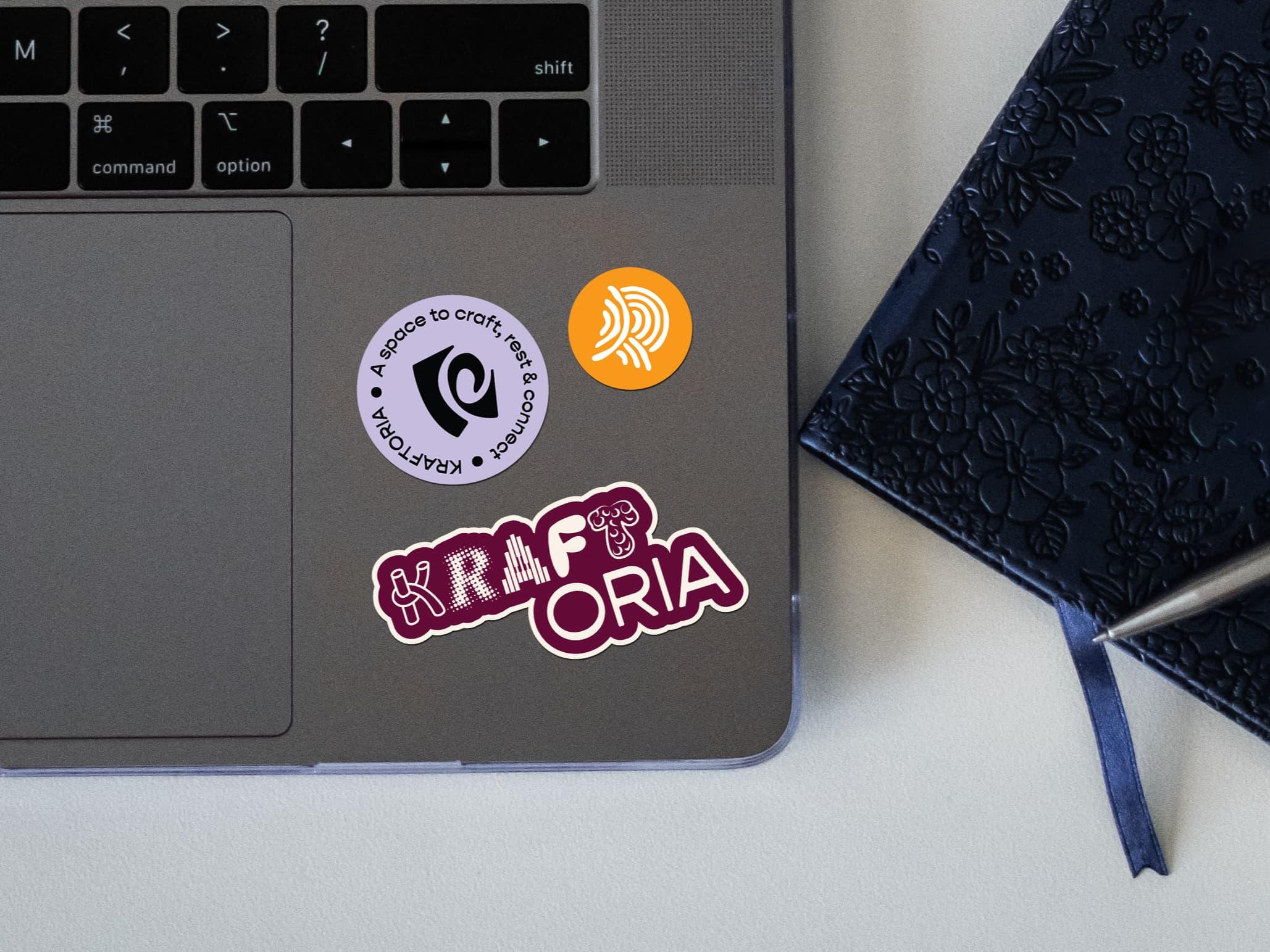 Kraftoria stickers on a laptop beside an embossed dark notebook.
