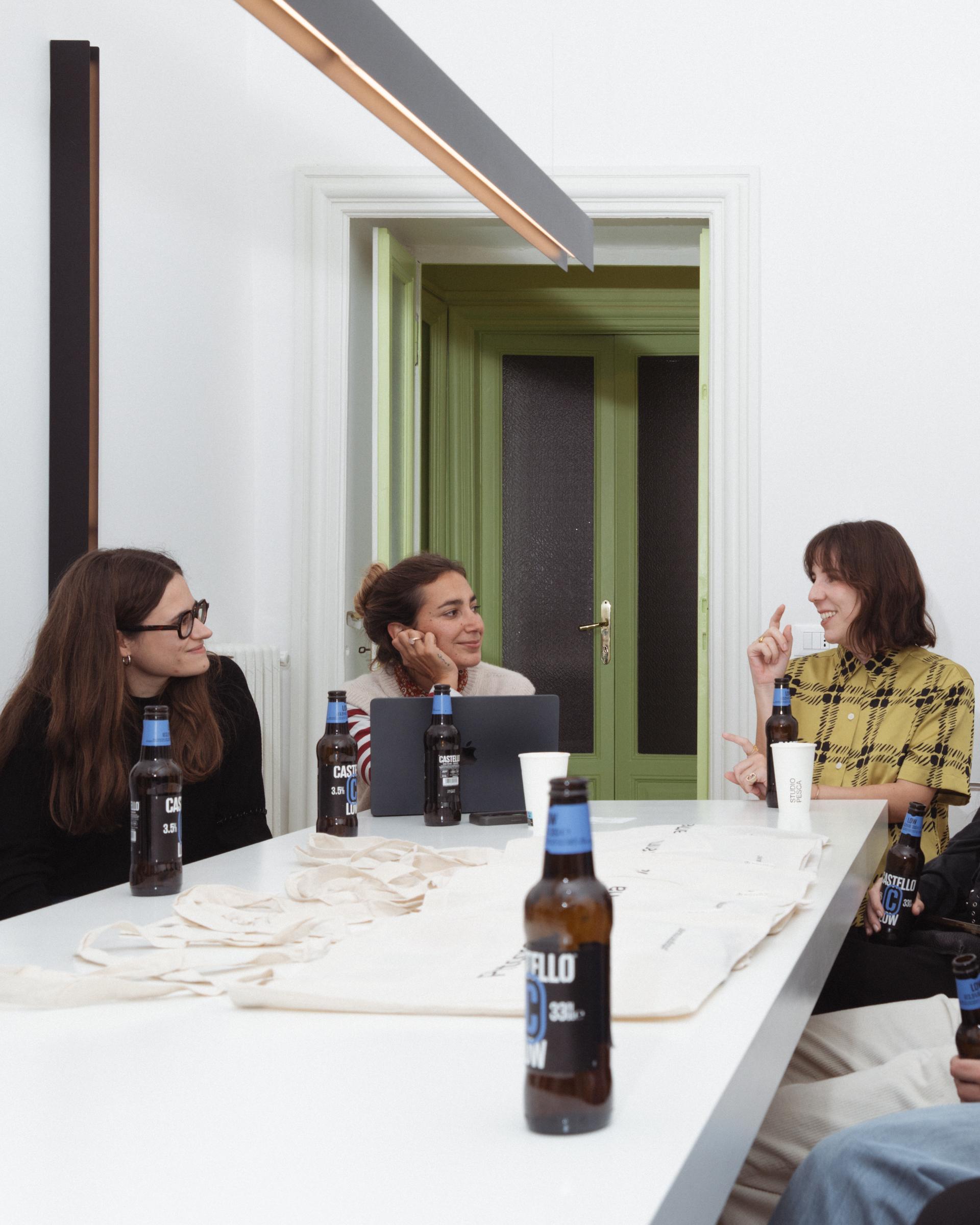 Three people talking around a table with bottles and cups during the Studio Pesca visit.