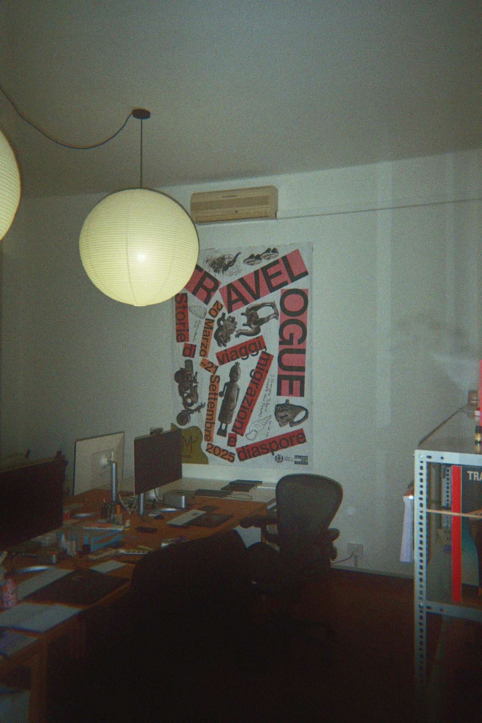 LaTigre studio desk beneath a poster, with two hanging paper lamps.