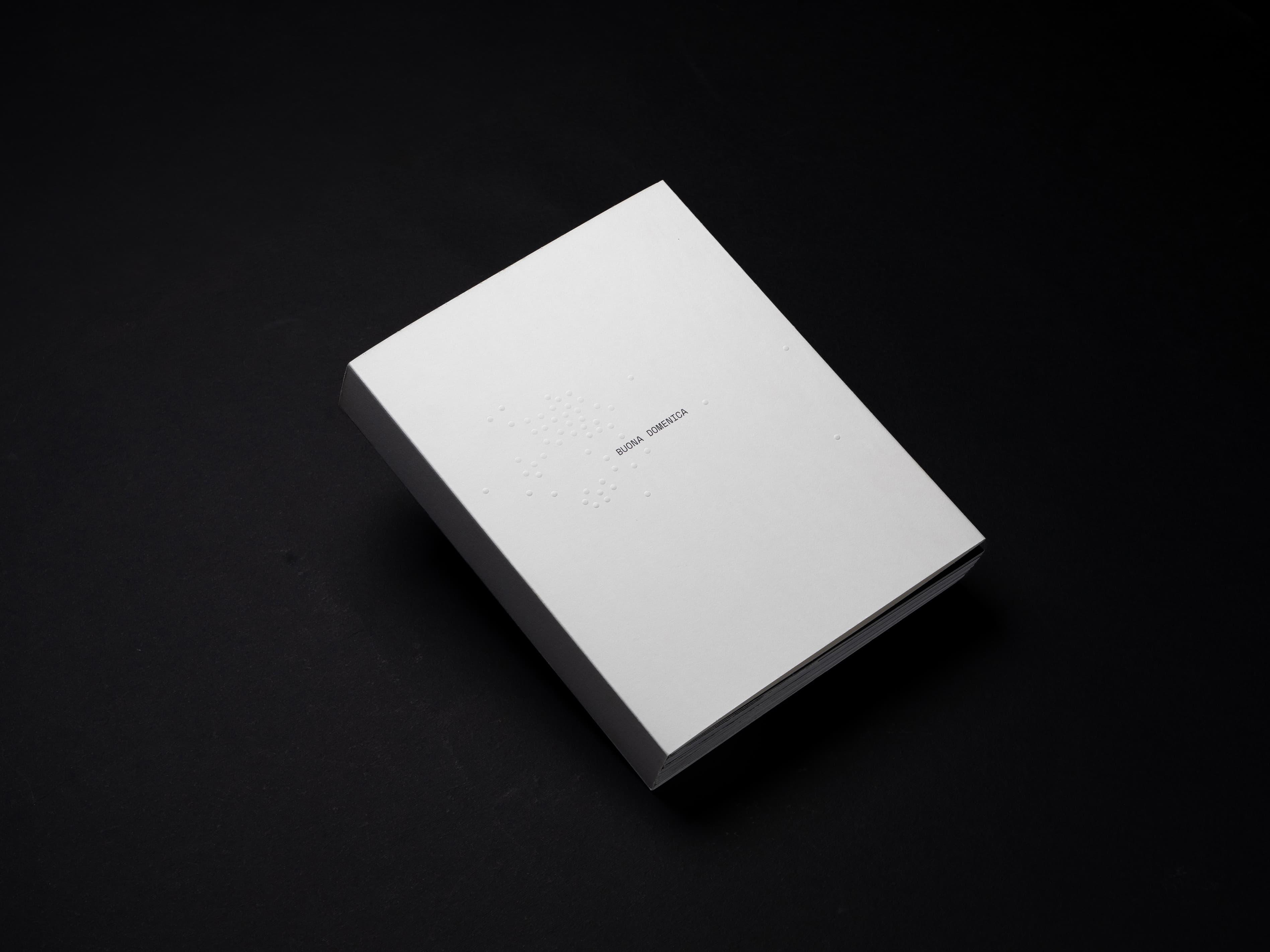 Plain white Buona Domenica book on a black background.