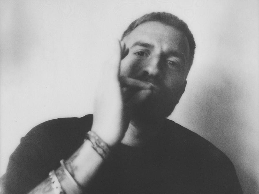 Grainy black-and-white portrait of a person resting their face on one hand.