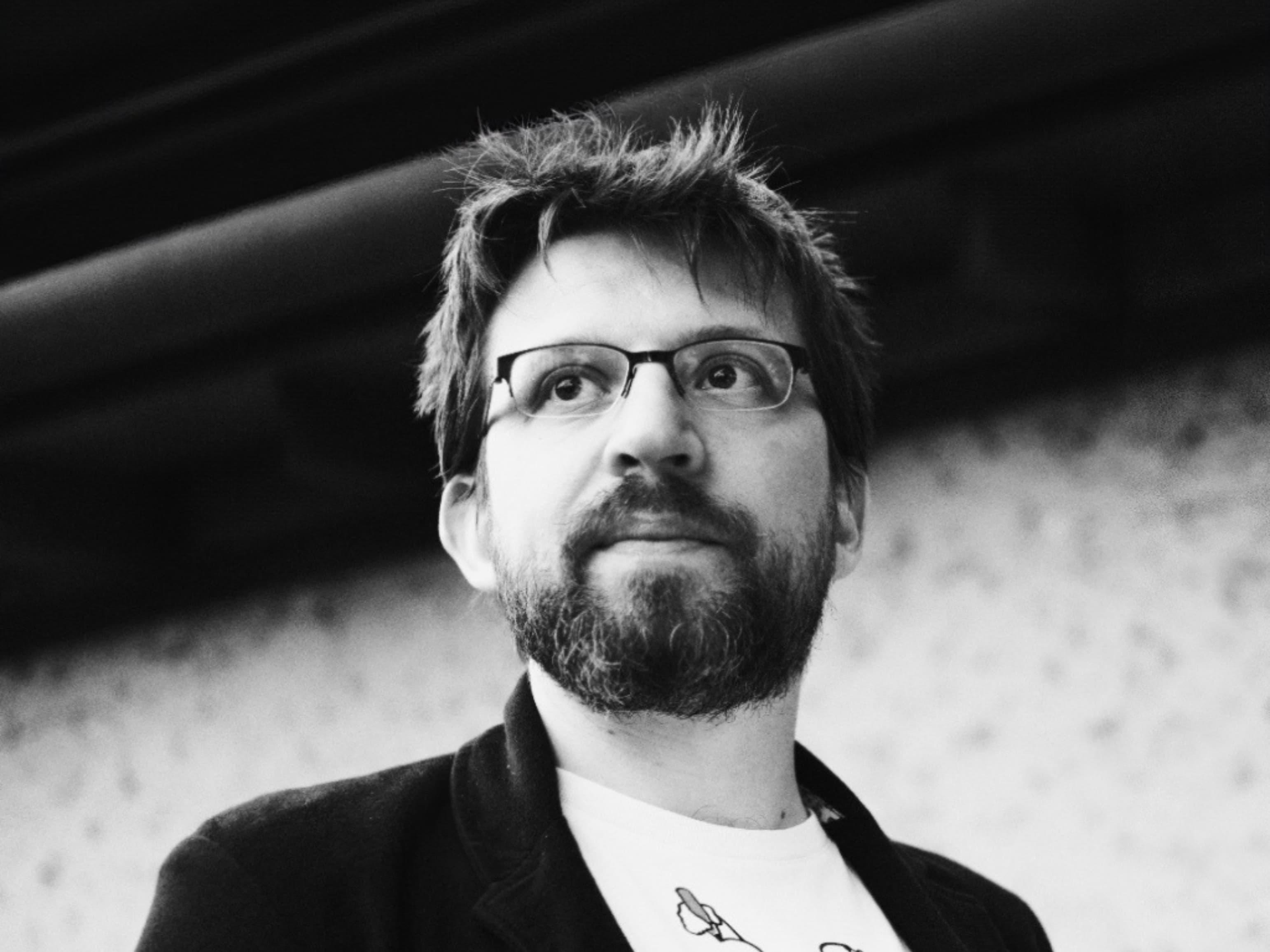 Black-and-white portrait of a person with glasses and a beard, photographed from below.