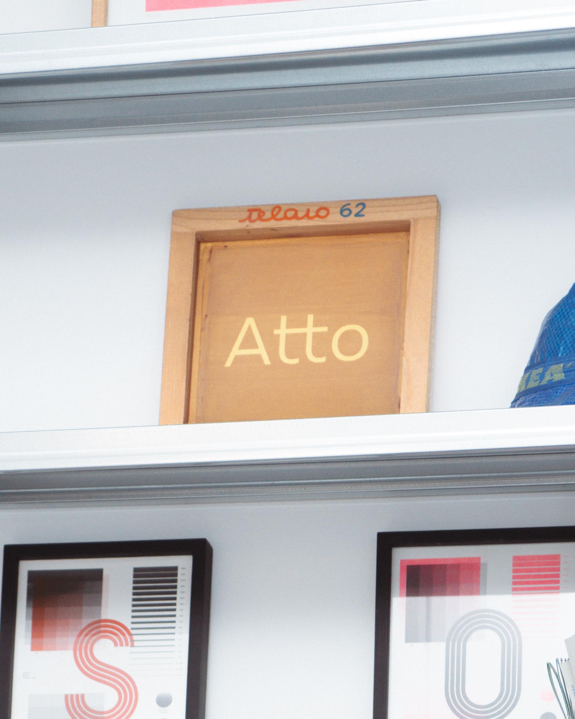 Atto sign and framed prints on a white studio shelf.