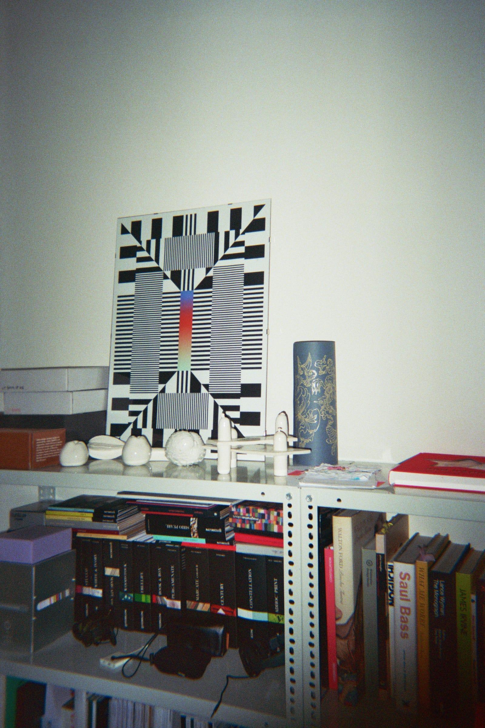 Books and printed objects on a white metal studio shelf.