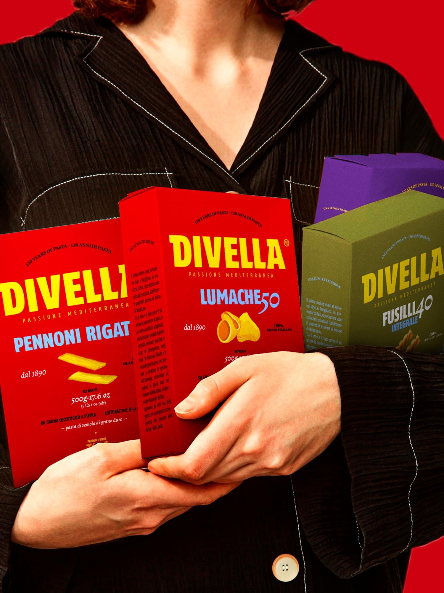 Person in black clothing holding three colorful Divella pasta packages.