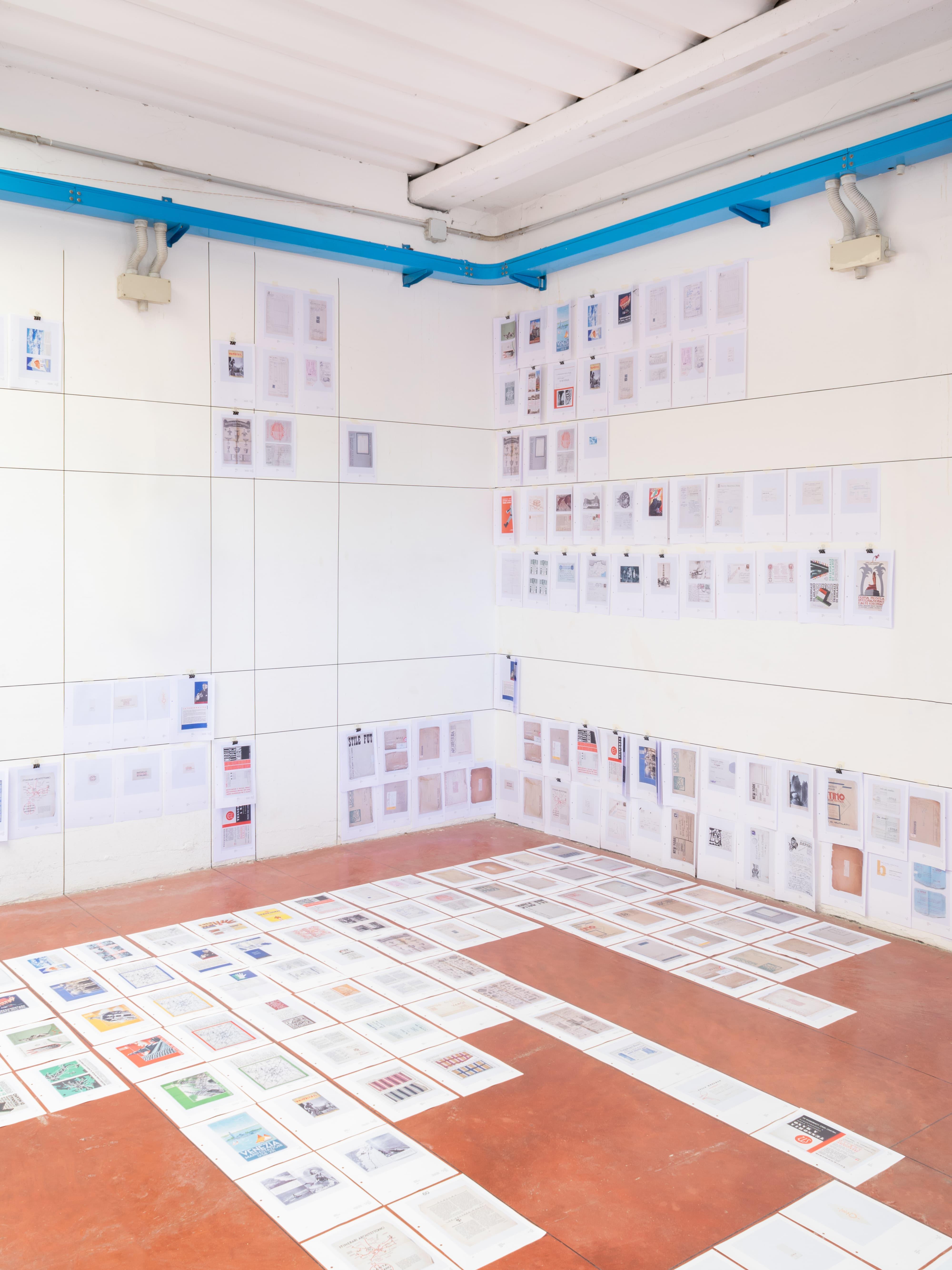 Installation view of an Ephemera exhibition with printed sheets arranged on walls and floor.