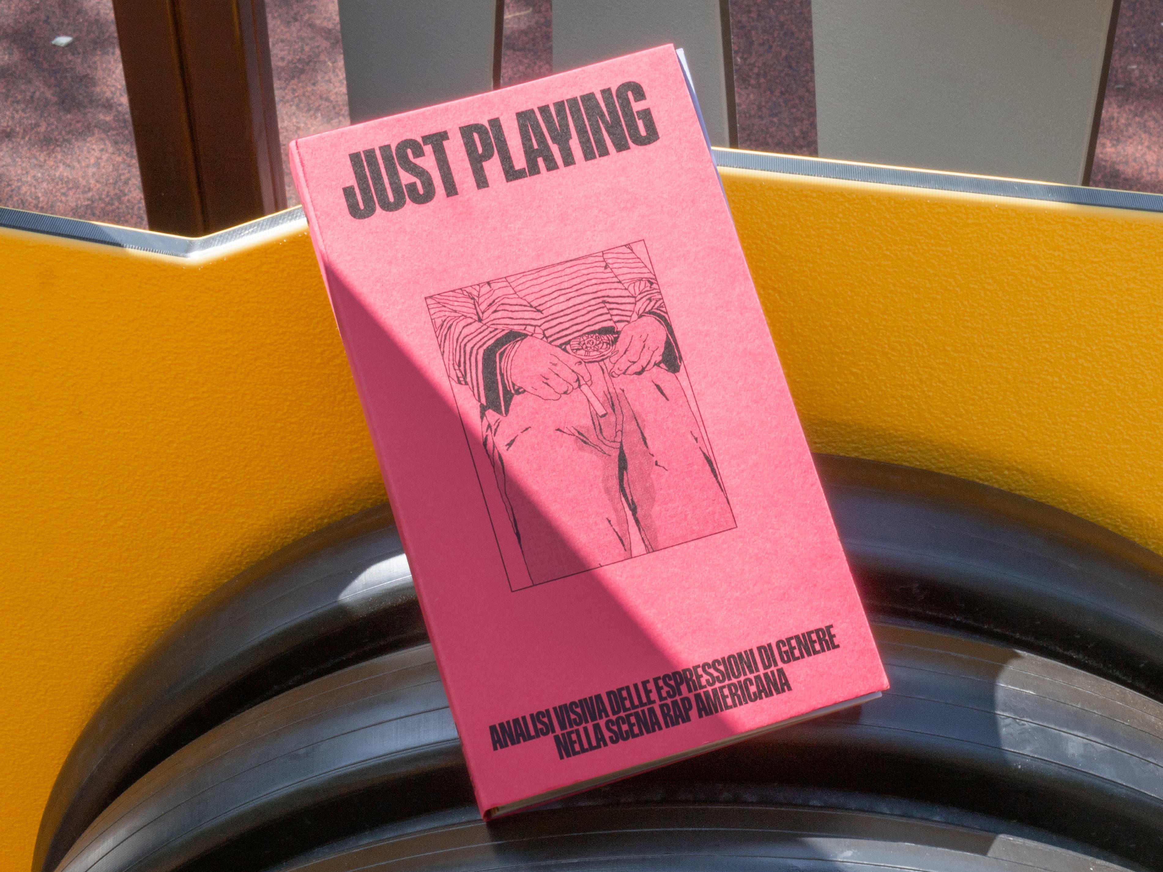 Pink Just Playing publication propped beside a yellow street barrier.