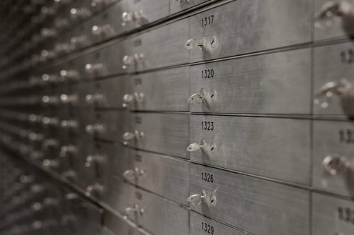 Rows of metallic safety deposit boxes with numbered labels and keyholes, creating a sense of security and organization, in a dimly lit space.