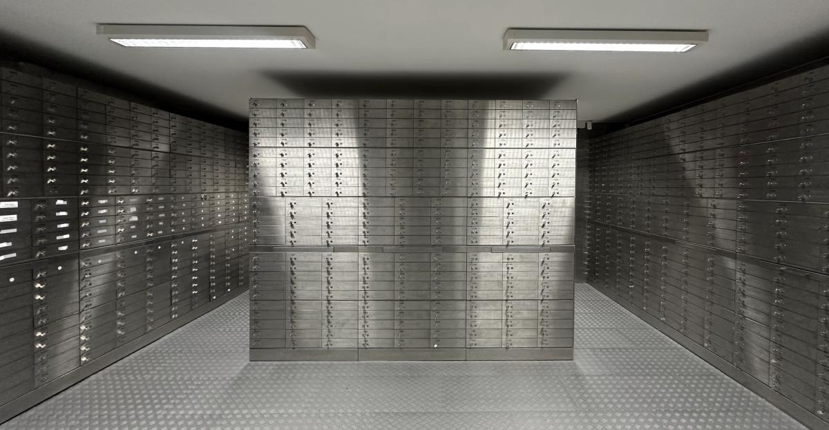Rows of metallic safety deposit boxes with small handles and keyholes, creating a sense of security and order in a dimly lit bank vault.