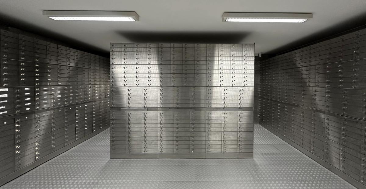 Rows of metallic safety deposit boxes with small handles and keyholes, creating a sense of security and order in a dimly lit bank vault.