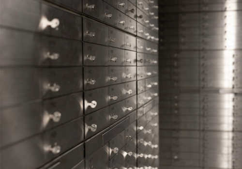 Rows of metallic safety deposit boxes in a dimly lit vault, each with a key inserted. The text "Store with us" conveys security and trust.