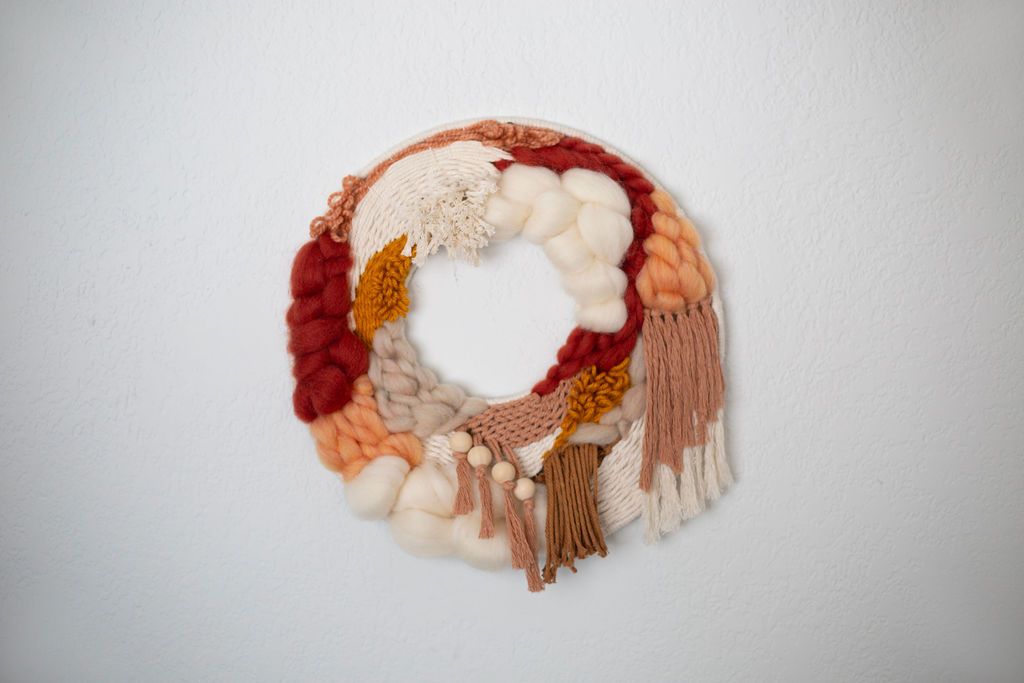 Round fiber wreath in red, rust, peach and cream with fringe