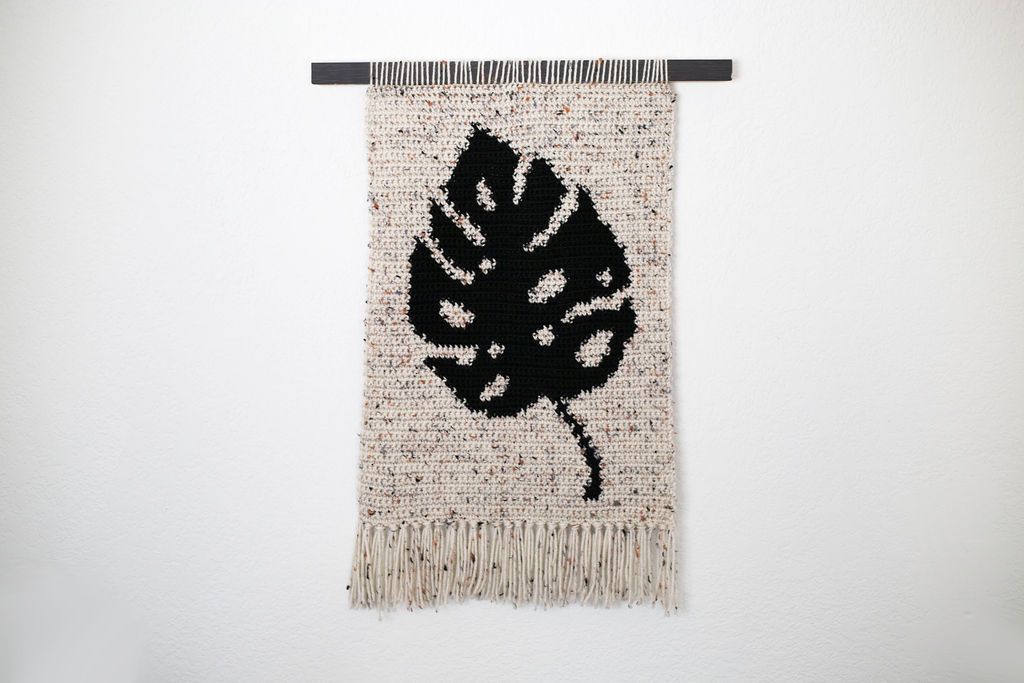 Speckled cream crochet tapestry with a black monstera leaf