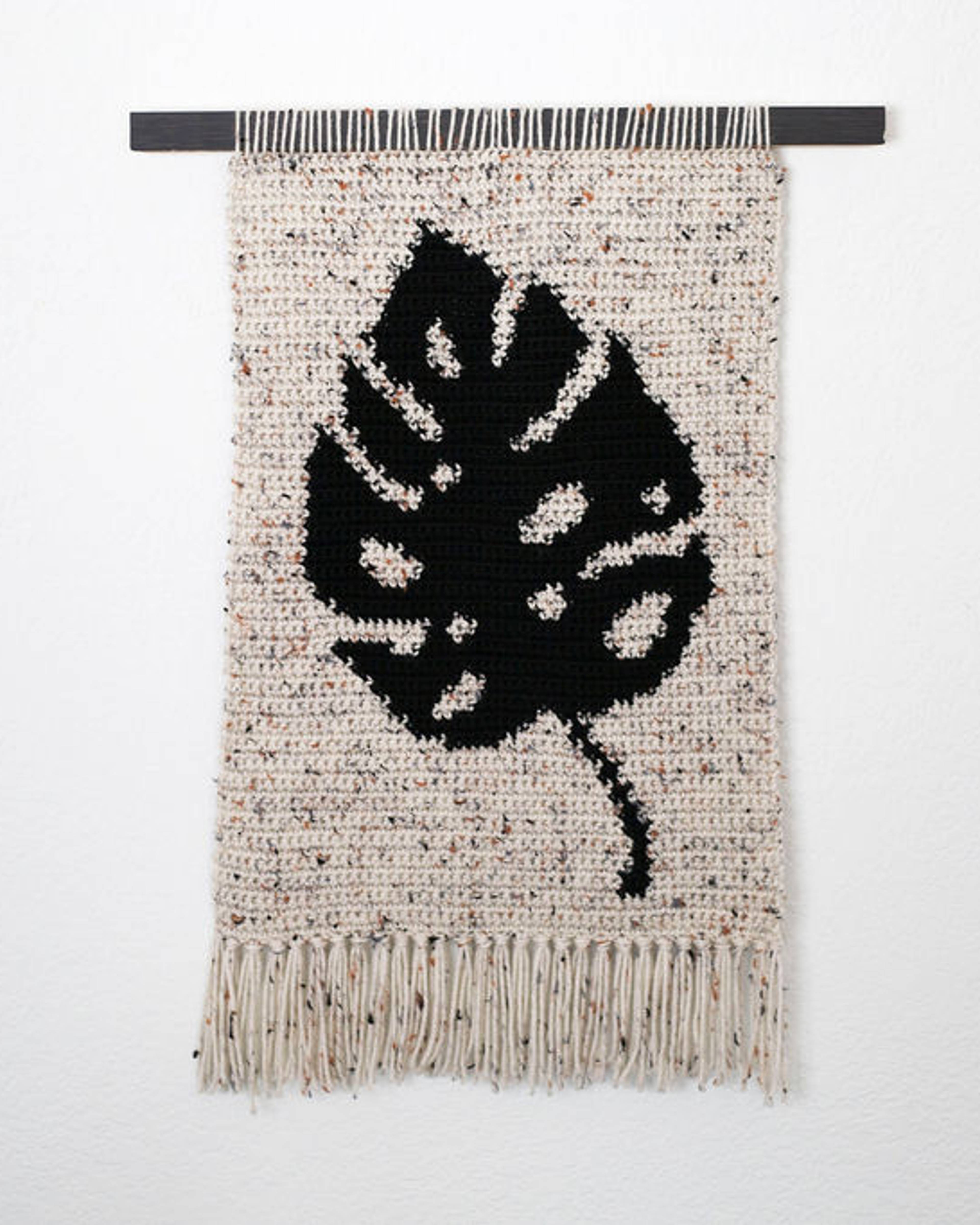 Speckled cream crochet tapestry with a black monstera leaf