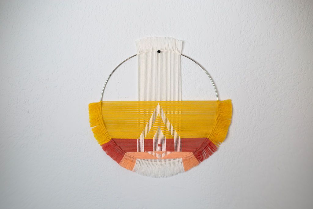 Half-moon weaving on a brass hoop in yellow, coral and white with a geometric motif