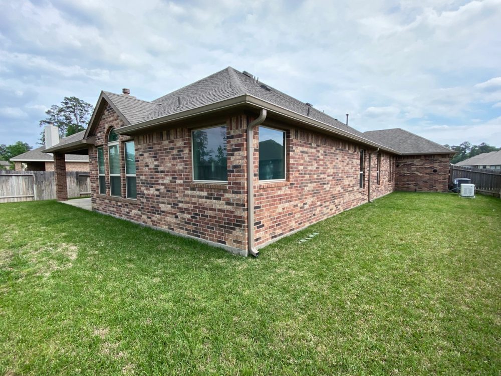 Light bronze seamless gutters and downspouts around the rear brick walls of a Foster's Ridge home