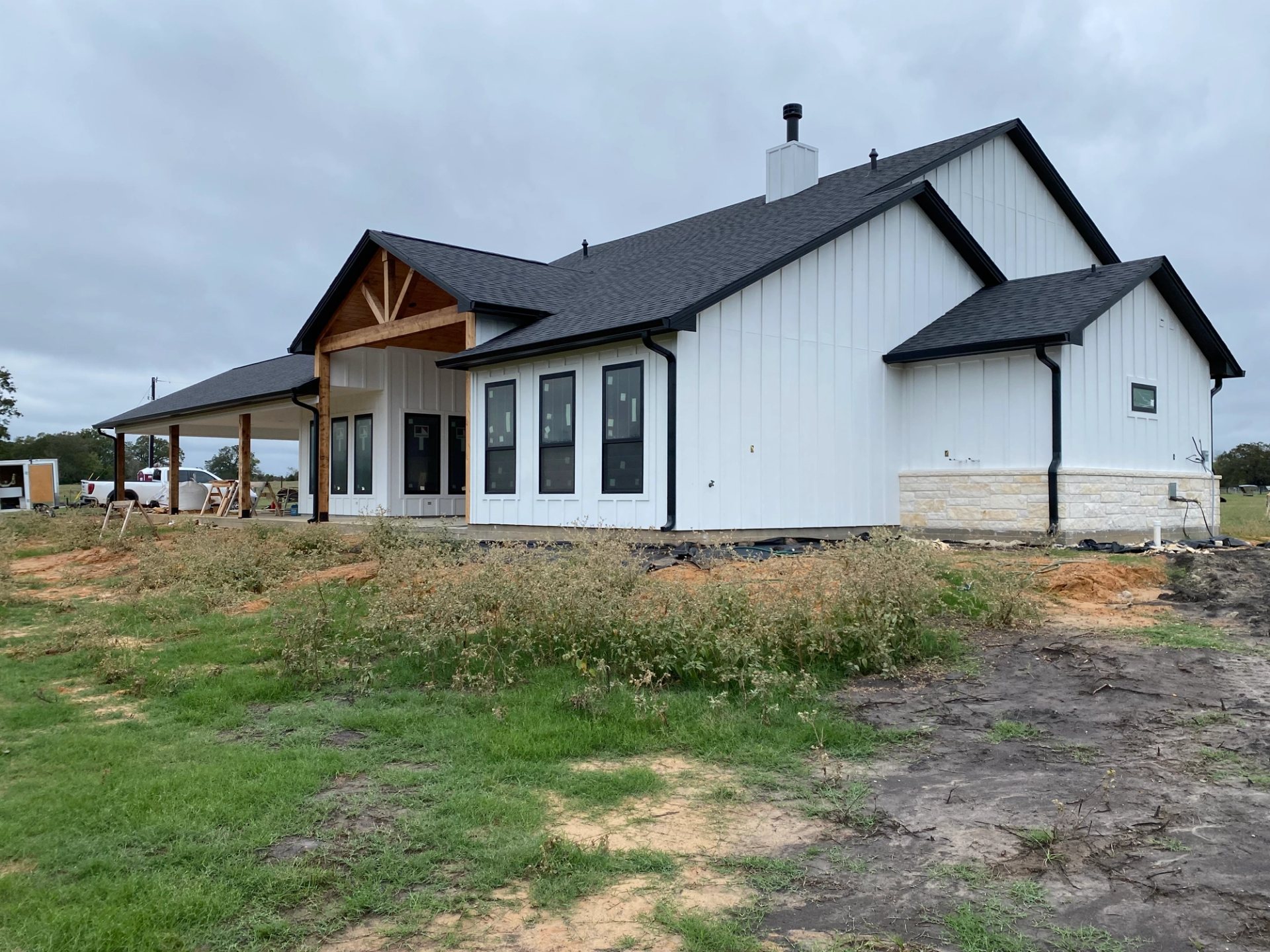 Black seamless gutters and downspouts outlining a white farmhouse with covered porches in North Zulch