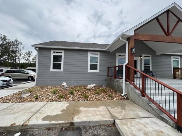 White seamless gutter and downspout beside the covered entrance and concrete access ramp of a gray commercial building