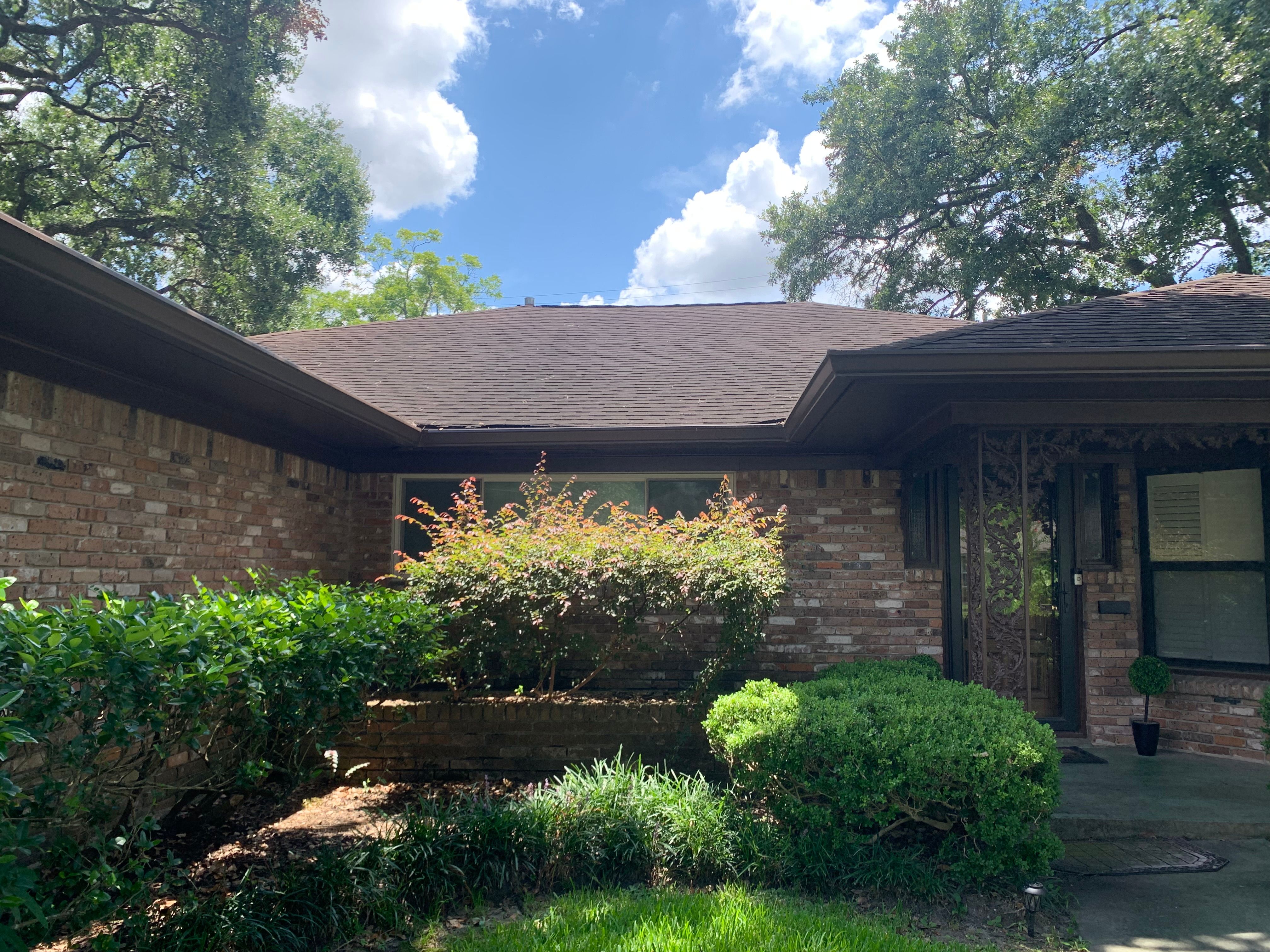 Brown seamless gutters across the front roofline of a landscaped Houston brick home