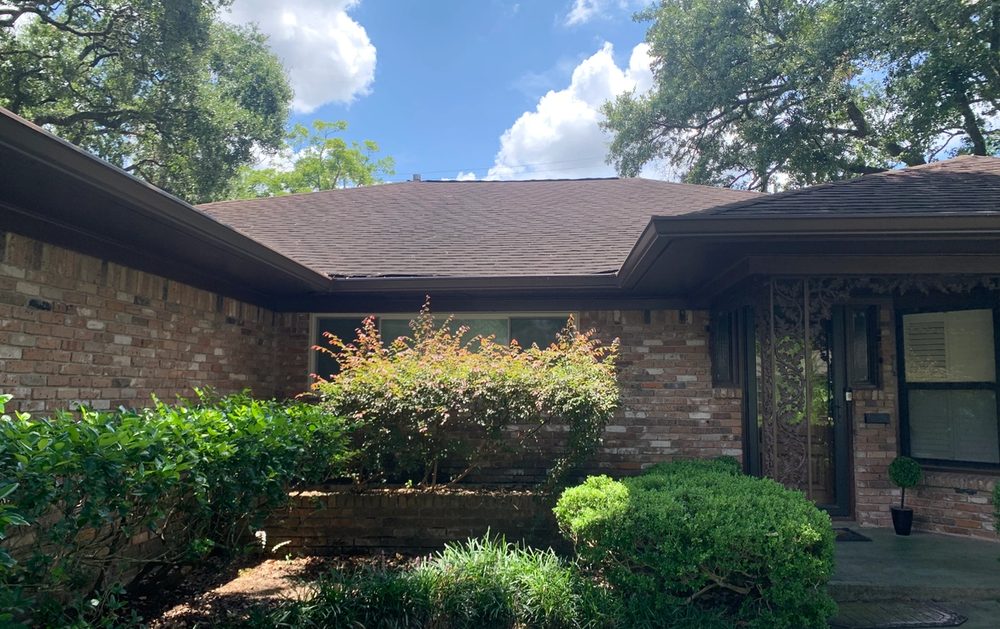Brown seamless gutters across the front roofline of a landscaped Houston brick home