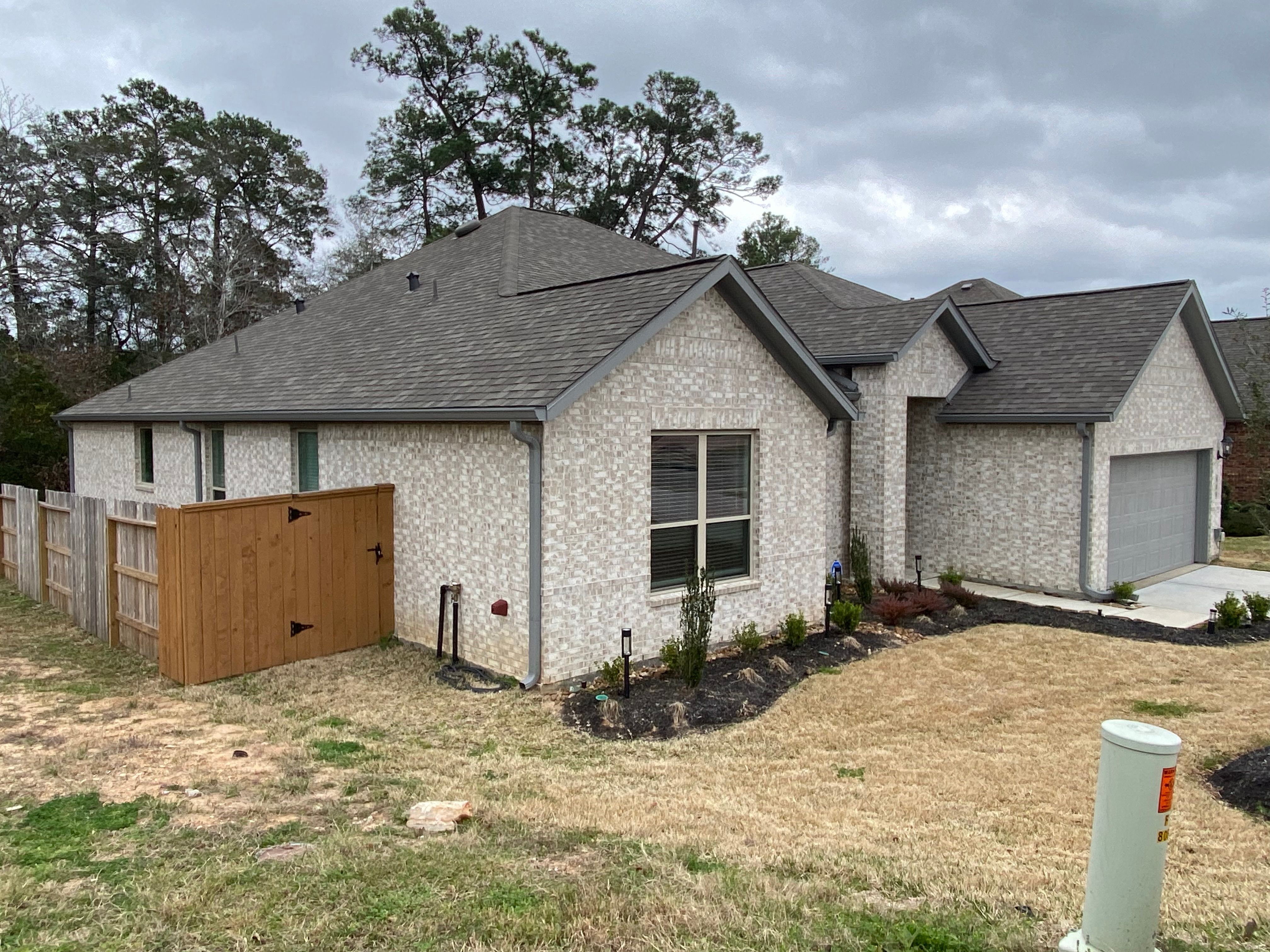 Dark gray seamless gutters and downspouts wrapping the light-brick front and side of a Conroe home