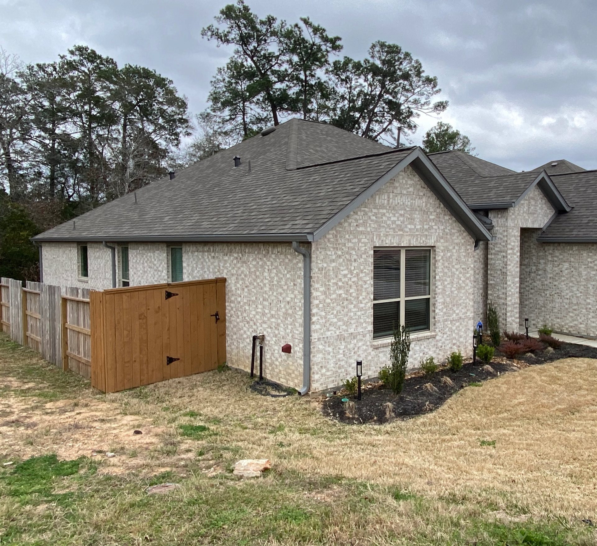 Dark gray seamless gutters and downspouts wrapping the light-brick front and side of a Conroe home