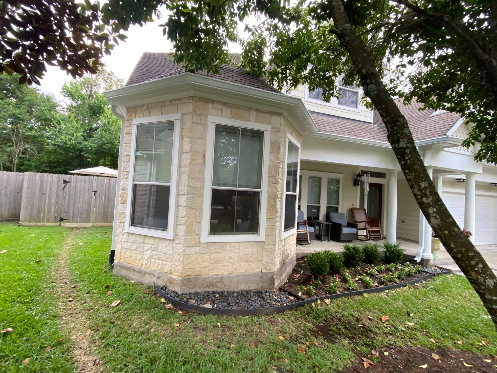 White gutters wrapping a stone-faced bay window under mature trees in Sterling Ridge, The Woodlands