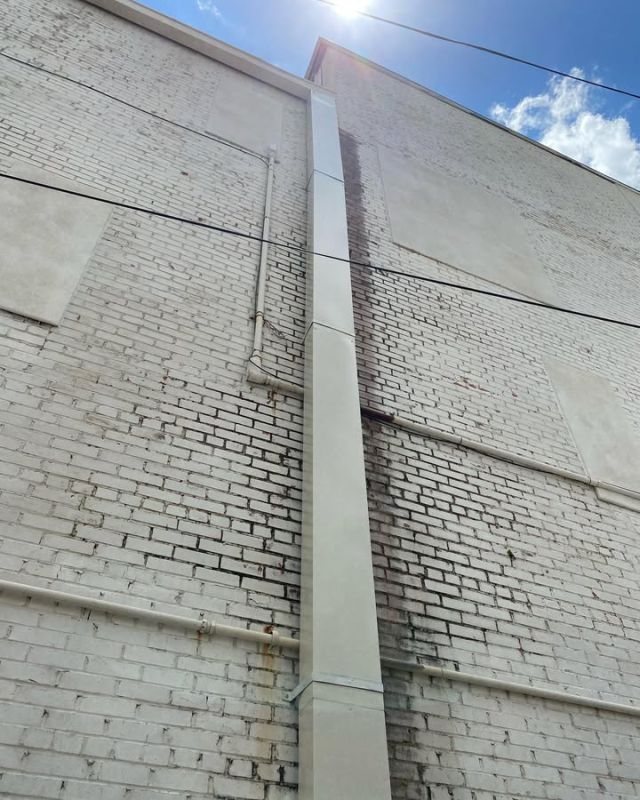 Tall light cream custom steel downspout on a painted-brick commercial wall in Downtown Conroe