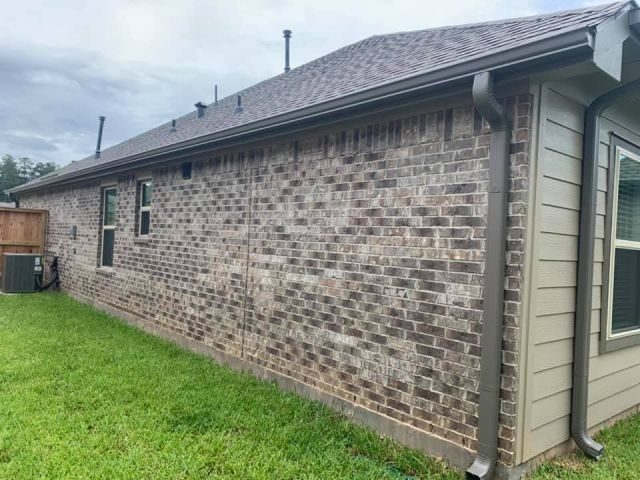 Light bronze seamless gutter and matching downspouts along the brick side of a new single-story home in Conroe