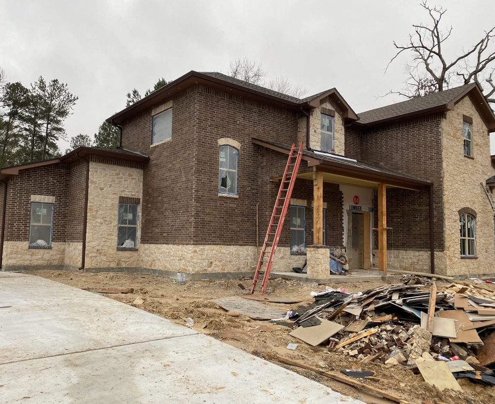 Brown seamless gutters and downspouts on the side of a new two-story brick home in Conroe