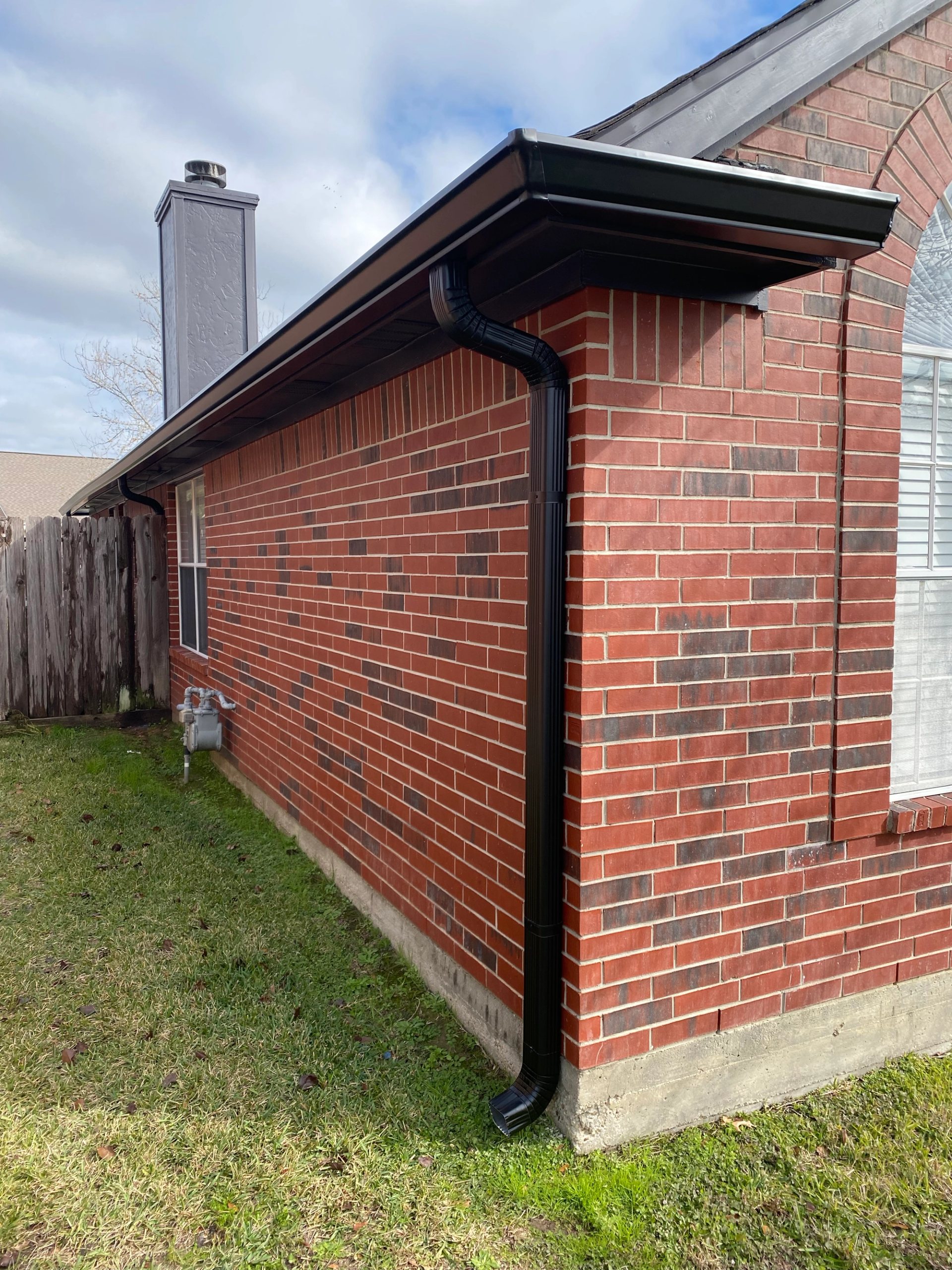 Black seamless gutter and matching downspout fitted to a red-brick corner on a Willis home