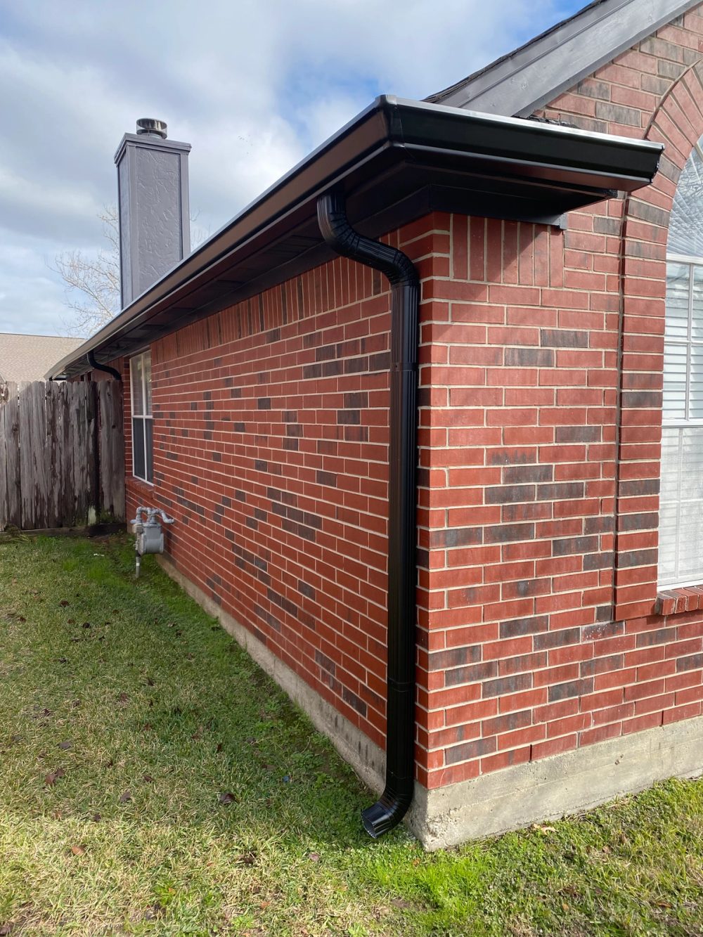 Black seamless gutter and matching downspout fitted to a red-brick corner on a Willis home