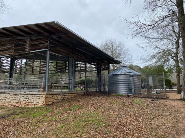 Open-sided Conroe park pavilion with a Galvalume box gutter and metal rainwater cistern beside the roofline
