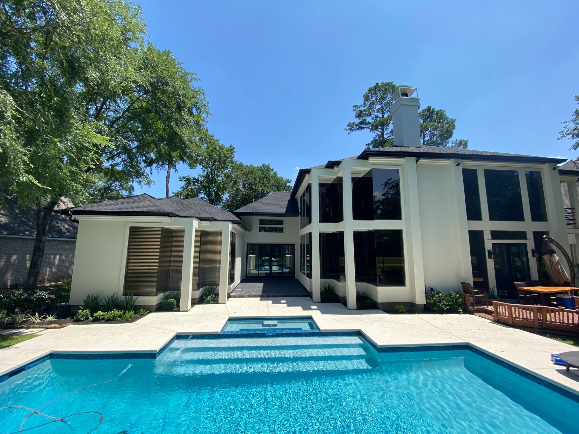 Black seamless gutters outlining a two-story white-stucco home and pool courtyard in Spring