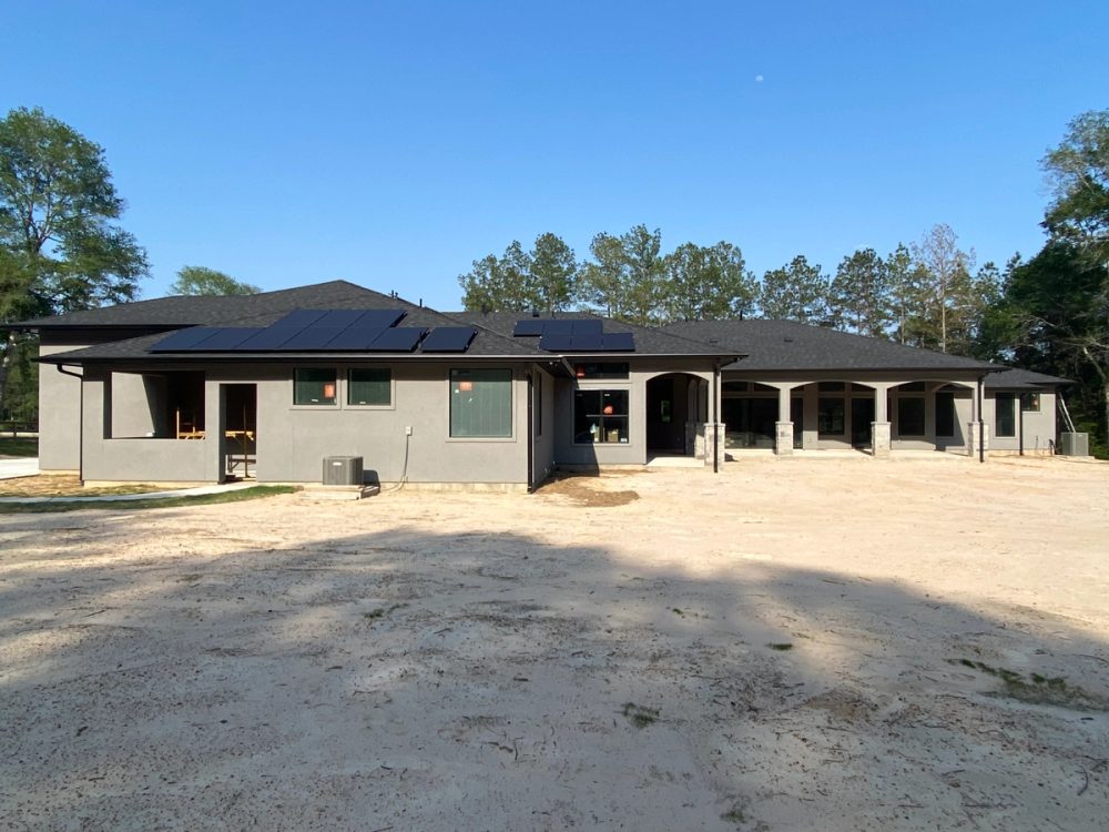 Black seamless gutters and downspouts spanning a broad gray-stucco rear elevation in Huntsville