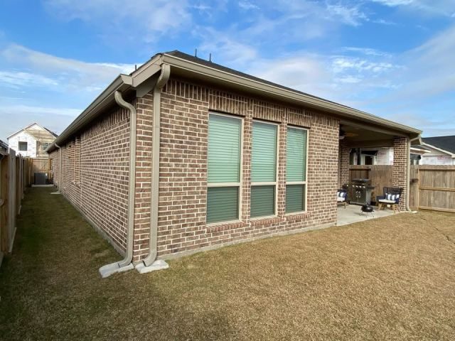 Clay seamless gutters and matching downspouts around the rear brick corner of a new Fulshear home
