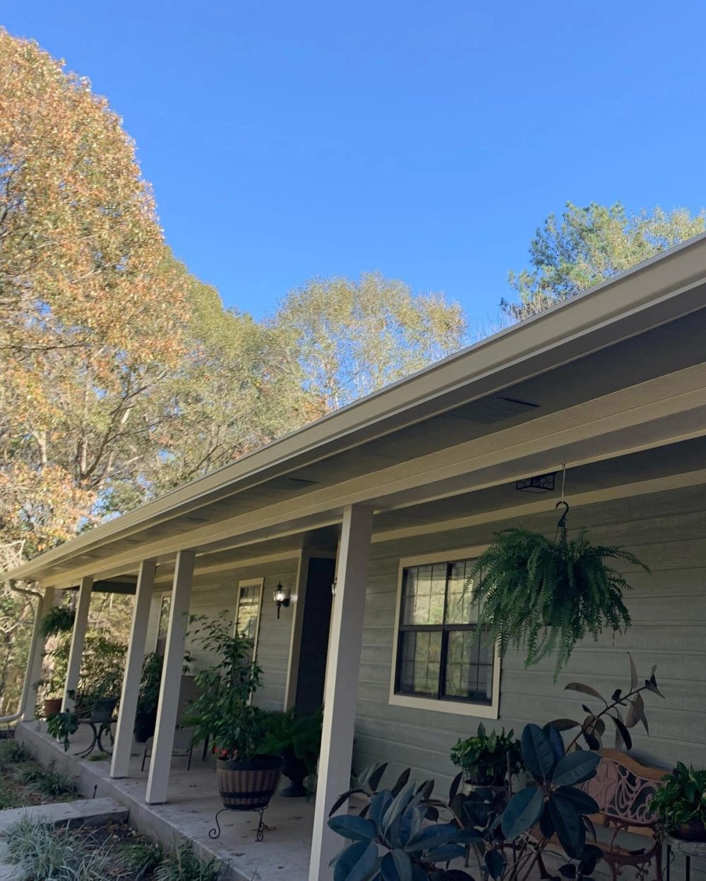 Cream seamless gutter running along the covered porch roofline of a gray-sided Conroe home