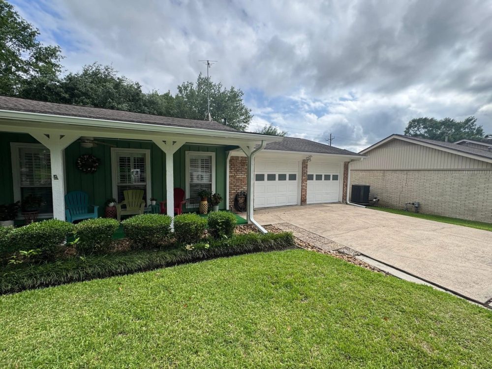 White seamless gutters and downspouts across the front porch and garage of a single-story Conroe brick home