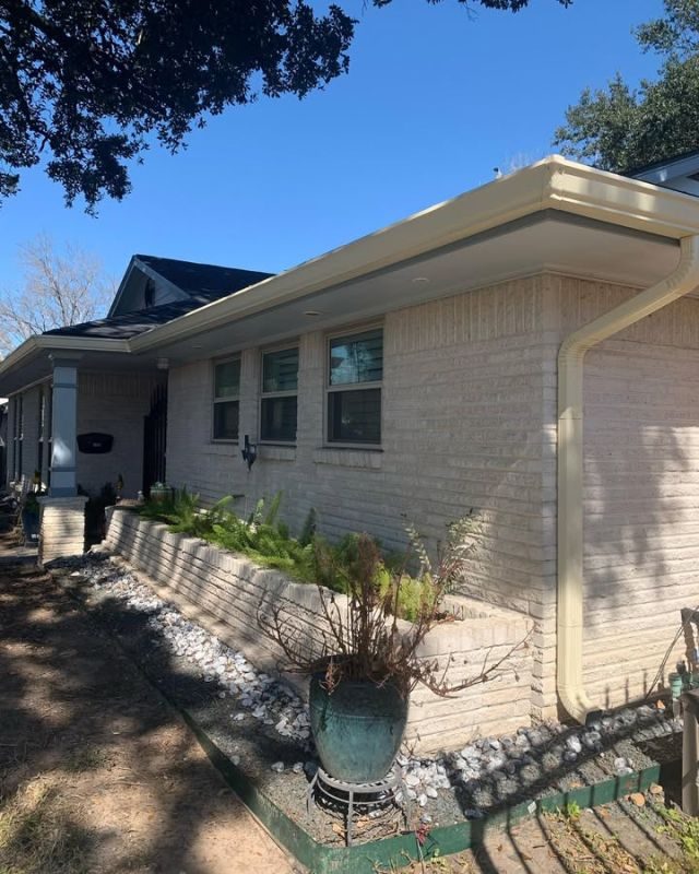 Light cream seamless gutter and downspout above a planted garden along a light-brick Houston home