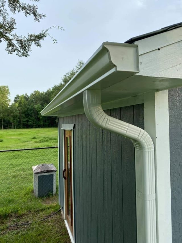 White seamless gutter and 3-by-4 downspout beside the door of a detached Conroe well house