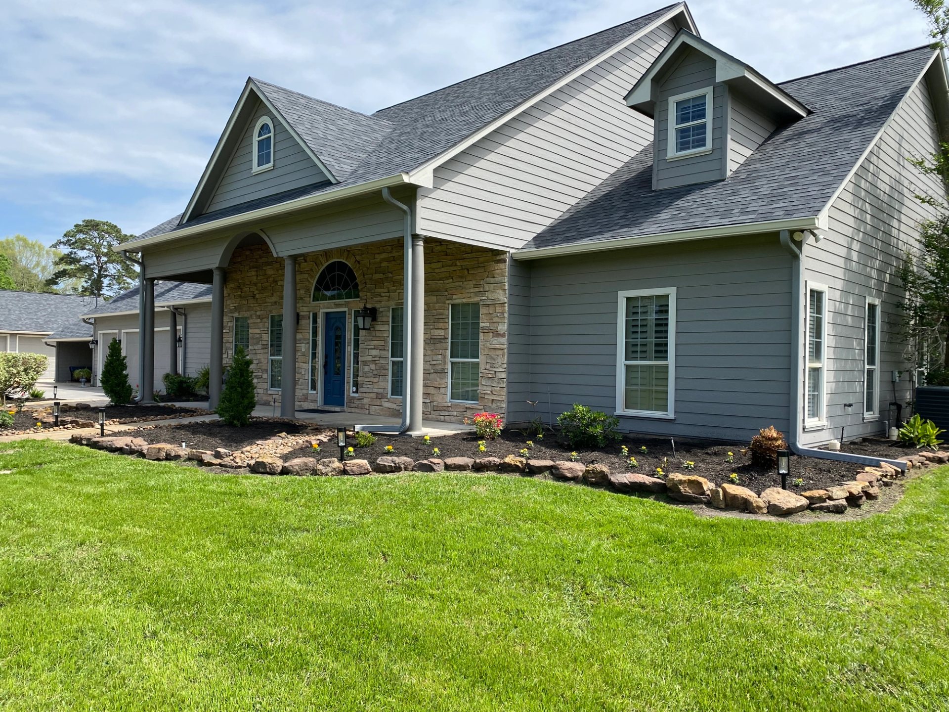 White seamless gutters and gray downspouts on the gabled front of a gray-and-stone Conroe home