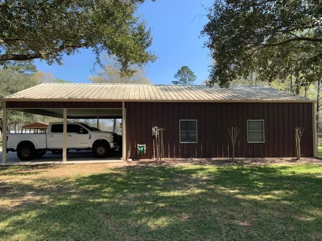 Detached brown metal shop in Conroe with cream seamless gutters and matching downspouts across the front roofline